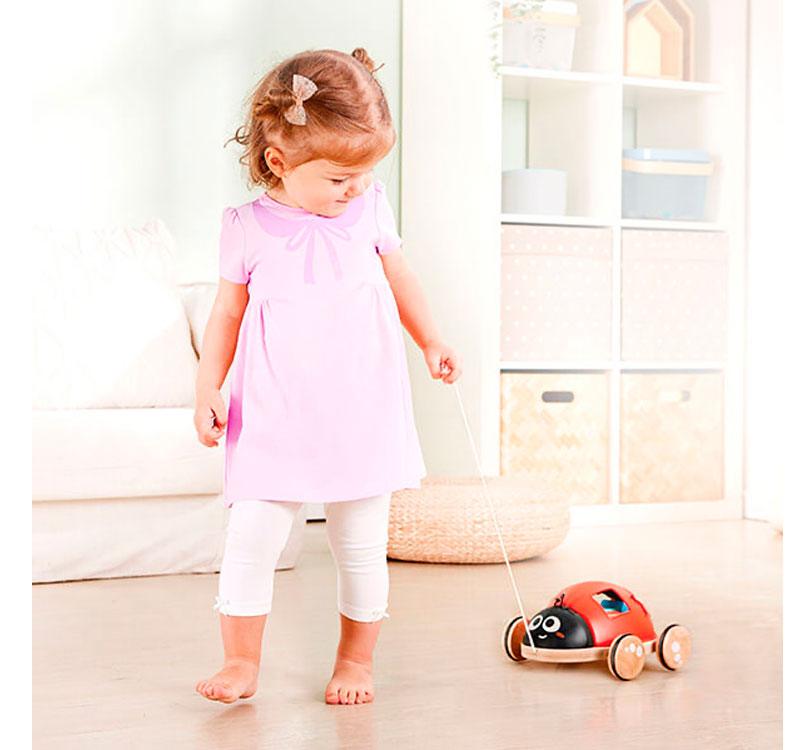 niña jugando con la mariquita a modo arrastre mariquita de madera clasificadora de formas de la marca Hape en color rojo y negro con bloques geométricos de colores brillantes