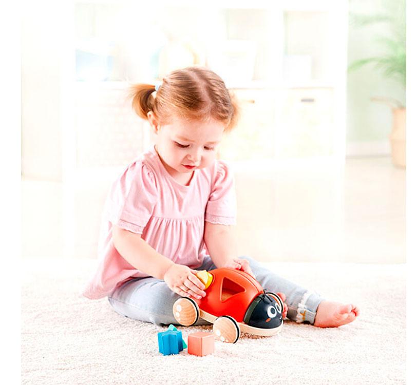 niña jugando con los bloques encajares de la mariquita de madera clasificadora de formas de la marca Hape en color rojo y negro con bloques geométricos de colores brillantes