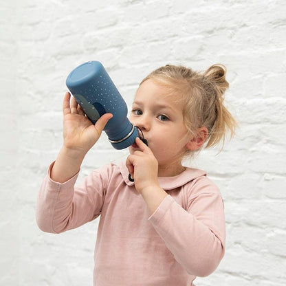 NIÑA BEBIENDO DE LA BOTELLA BOTELLA DE ACERO DE LA MARCA TRIXIE DE FORMA CILINDRICA CON TAPON DE PITORRO AL TONO, MODELO ELEFANTE EN COLOR AZUL DENIM