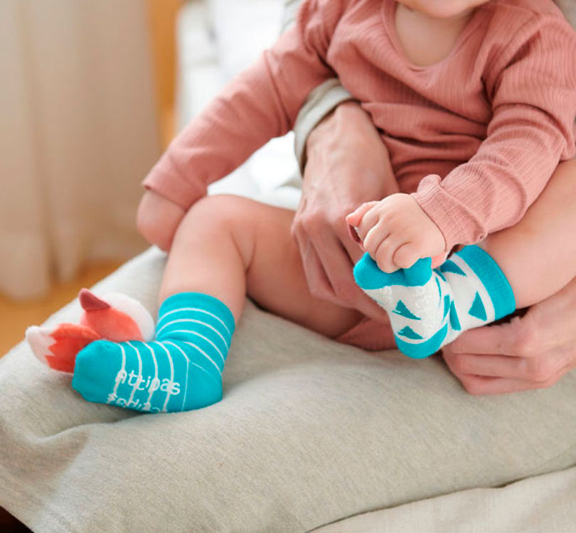 os calcetines de estimulación Attipas. A través de sus colores, sonidos y texturas llamativos, el bebé no solo se divierte, sino que también fomenta su desarrollo en estas áreas. bebe con calcetines de zorro