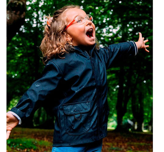 foto niña lifestyle en el campo chubasquero Euri en color azul marino brillante diseño  en color azul marino impermeable. Los bolsillos frontales son súper prácticos, y el forro interior a rayas marinero añade un toque de estilo de lo más molón