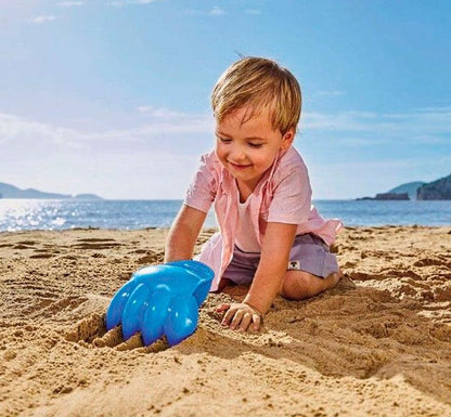 foto de niño en plan playa jugando con ¡Descubre el increíble rastrillo con forma de pata gigante! ¡Robusto, divertido y de un vibrante color azul brillante! Ideal para jugar en la arena y cavar agujeros inmensos y gigantes, ¡al igual que el rastrillo mismo.!