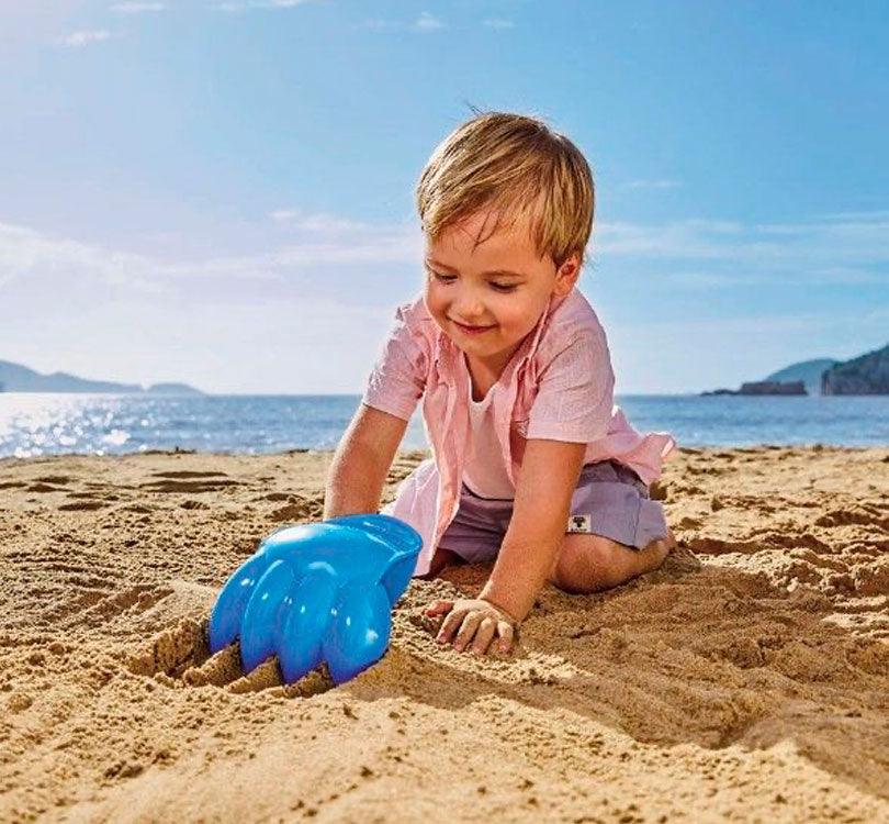 foto de niño en plan playa jugando con ¡Descubre el increíble rastrillo con forma de pata gigante! ¡Robusto, divertido y de un vibrante color azul brillante! Ideal para jugar en la arena y cavar agujeros inmensos y gigantes, ¡al igual que el rastrillo mismo.!
