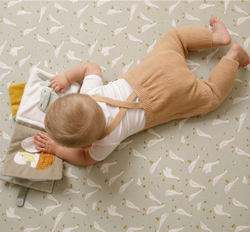 Niño en el suelo jugado con el Libro blandito de actividades ocas de Little Dutch con el bordado de una oca sobre fondo en color menta de la marca Little Dutch