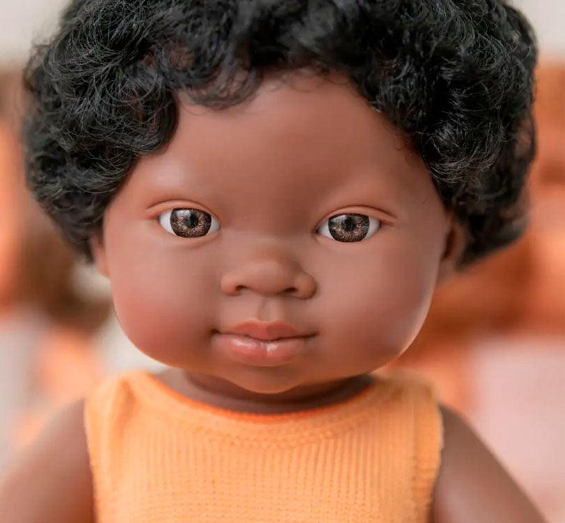 primer plano de la muñeca es una niña africana con un adorable pelele mostaza. Perfumadas ligeramente a vainilla, ¡son irresistiblemente achuchables! Hechas con cariño y al 100% en España,