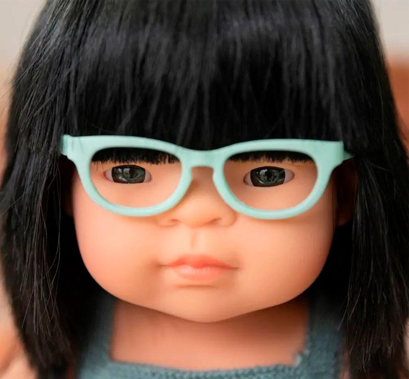 primer plano Esta muñeca es una niña asiática con pelo liso negro y gafas,  con un adorable pelele azul petróleo. Perfumadas ligeramente a vainilla, 