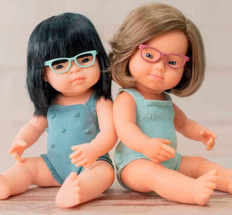 Esta muñeca es una niña asiática con pelo liso negro y gafas,  con un adorable pelele azul petróleo. Perfumadas ligeramente a vainilla,  lifestyle con otra muñeca con Síndrome Down