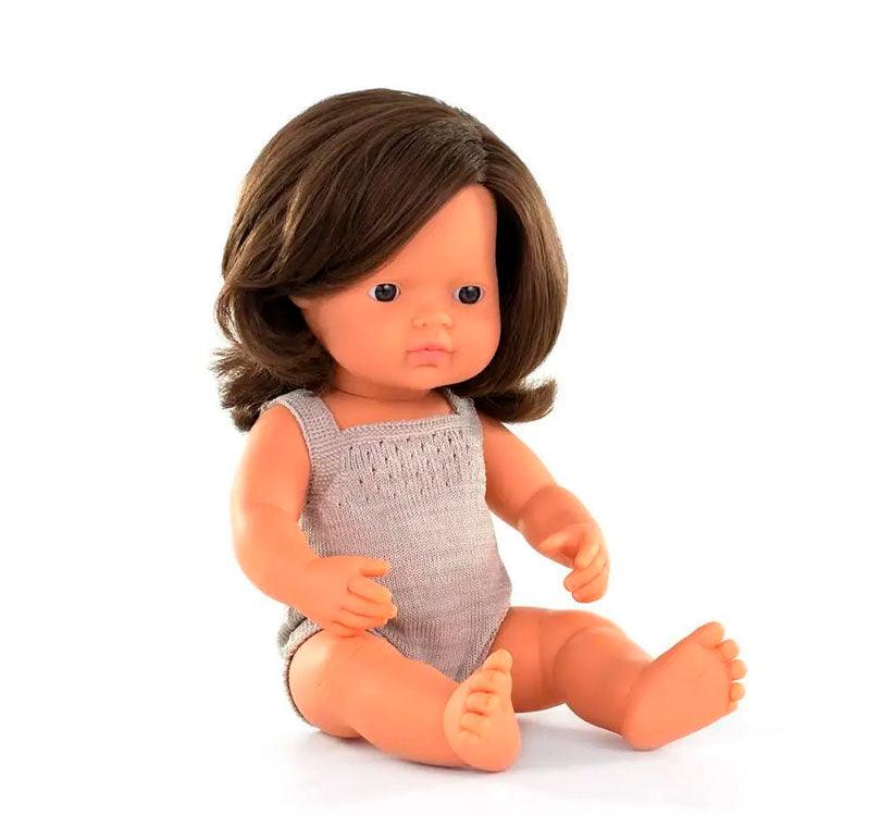 muñeca es una niña  caucásica con pelo liso castaño, con un adorable pelele gris topo sentada Miniland