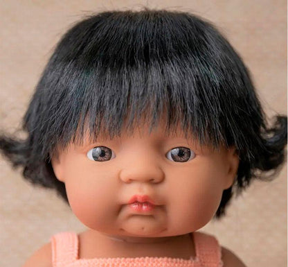 primer plano Esta muñeca es una niña latinoamericana con pelo castaño oscuro liso, con un adorable pelele albaricoque marca Miniland