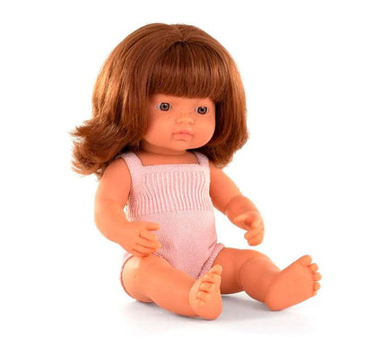 Sentada niña caucásica con pelo pelirrojo liso castaño , con un adorable pelele rosa claro marca Miniland