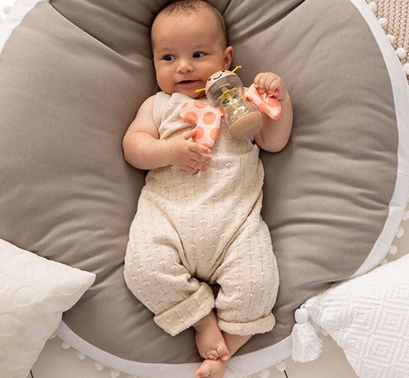 niños jugando en la cama con la Palo de lluvia de la marca Hape con bordes de madera con cuerpo transparente y alitas de estampado de lunares color salmón