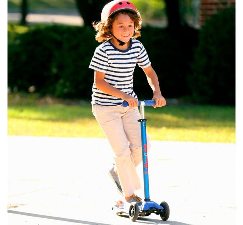 niño montando en el patinete maxi deluxe led en color azil con detalles en rojo en la plataforma de la marca micro