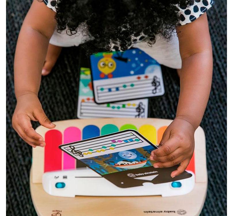 foto desde arriba de niña con el pelo moreno y rizado tocando el piano de madera de la marca hay y la colección Magic touch con las teclas de colorines y partituras en cartón con los colores de las teclas