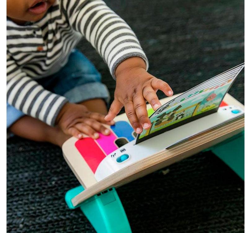 vista lateral de niño sentado jugando con piano de madera de la marca hay y la colección Magic touch con las teclas de colorines y partituras en cartón con los colores de las teclas