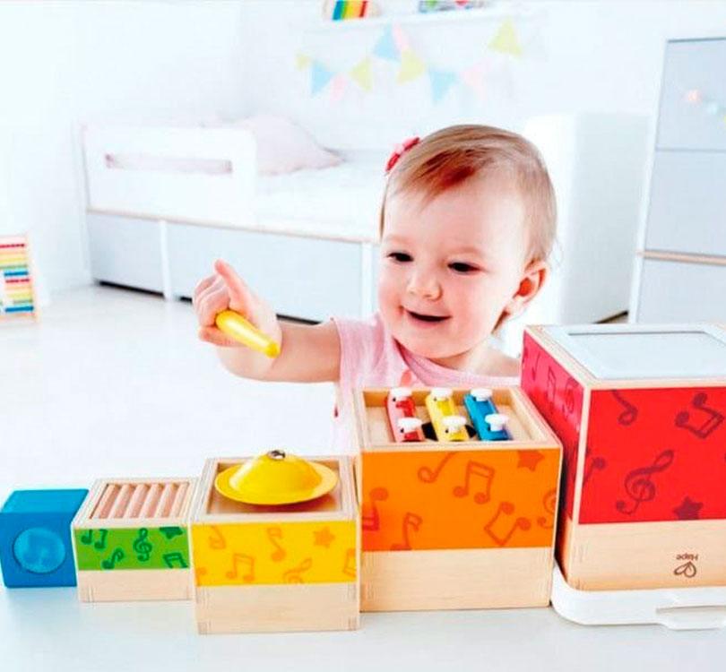 niña jugando con las cajas en fila de la Torre apiladle musical Hape con 5 cajas de madera apiladles con diferentes instrumentos musicales  de HAPE en color madera natural combinada con colores brillantes