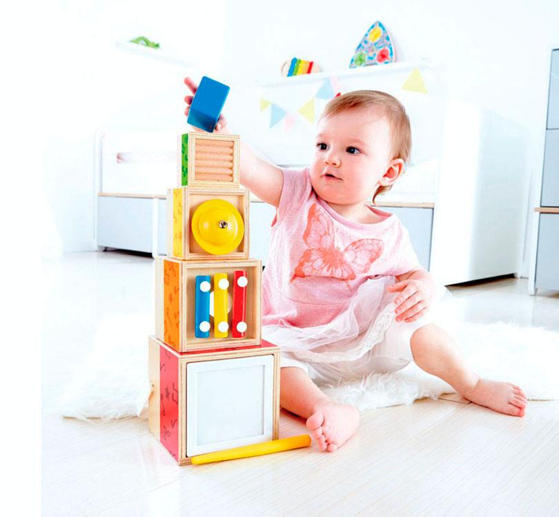 Niña jugando con las cajas apiladas de la Torre apiladle musical Hape con 5 cajas de madera apiladles con diferentes instrumentos musicales  de HAPE en color madera natural combinada con colores brillantes