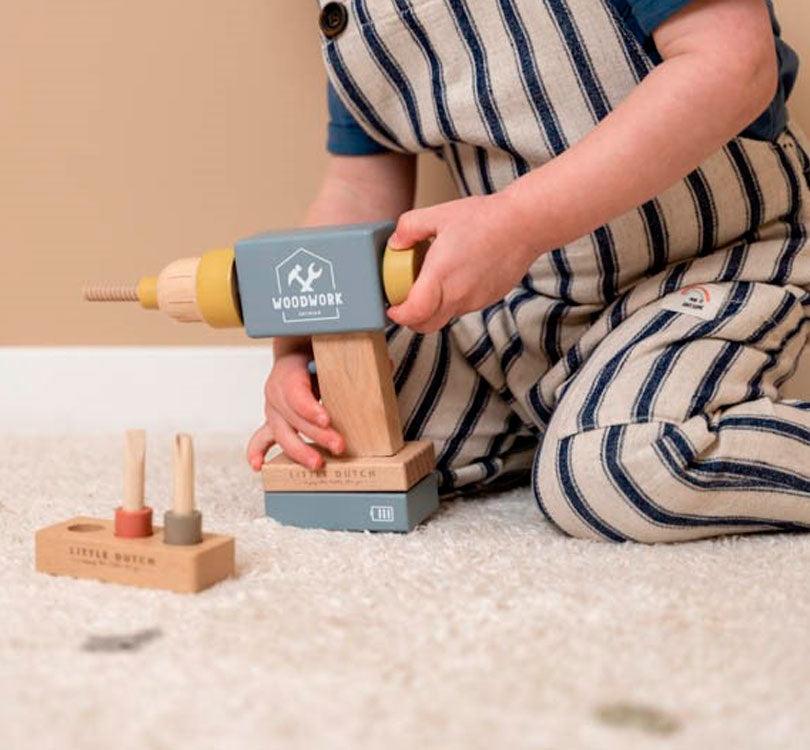 niño sentado en la alfombra jugando con el taladro de madera fsc en colores nórdicos con tres brocas intercambiables de Little dutch  Editar texto alternativo