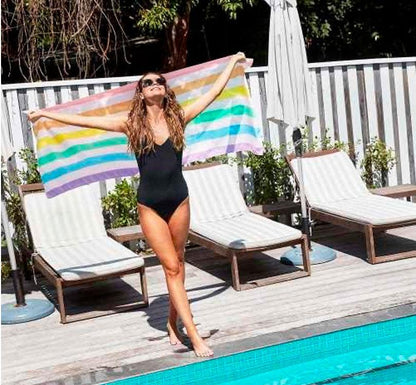 chica en la piscina cn los brazos abiertos con la Toalla antiarena marca dock and bay con estampado de rayas verticales en colores el arcoiris modelo rainbow pastel talla L