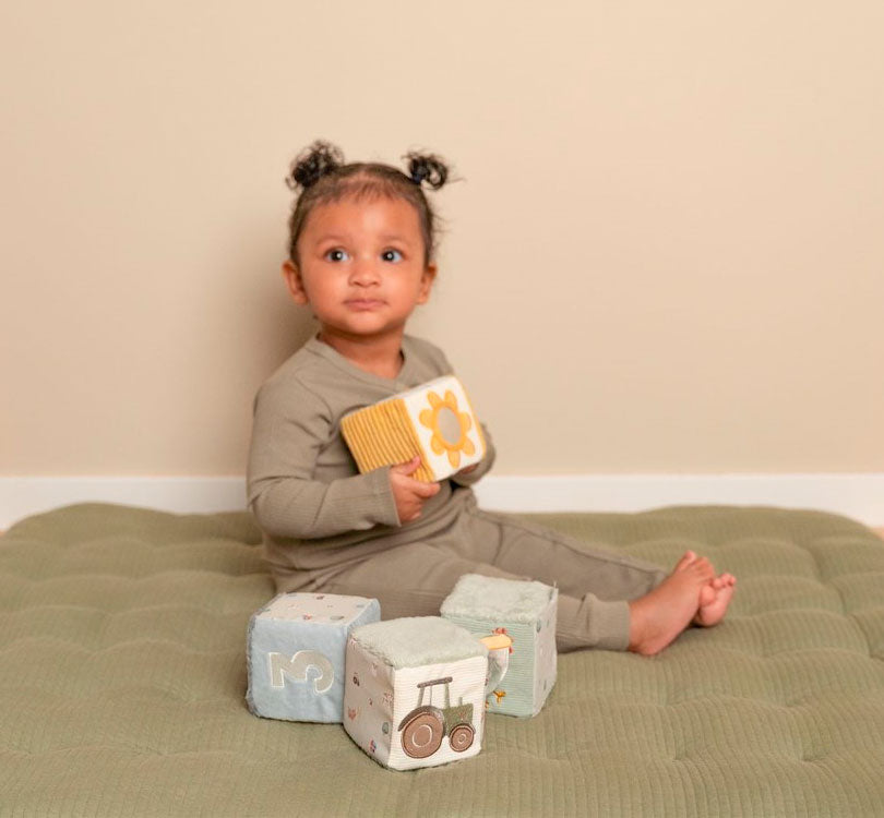 niña jugando con onjunto de cubos blanditos de la colección Pequeña Granja.  Estimula la coordinación mano-ojo de tu pequeño mientras se divierte durante horas. Con 4 cubos sensoriales, cada uno diseñado con colores suaves y un número único, tu bebé también podrá explorar divertidas etiquetas, caras de felpa y un espejo soleado.