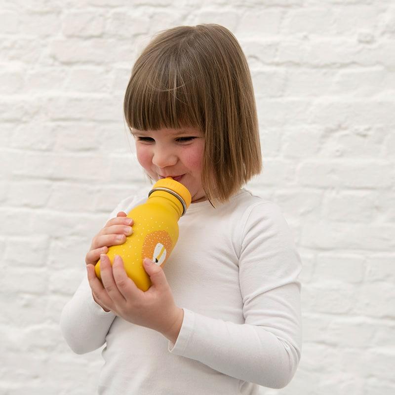 Foto de lifestyle  de niña bebiendo agua  BOTELLA DE ACERO DE LA MARCA TRIXIE DE FORMA CILINDRICA CON TAPON DE PITORRO AL TONO, MODELO LEON EN COLOR AMARILLO