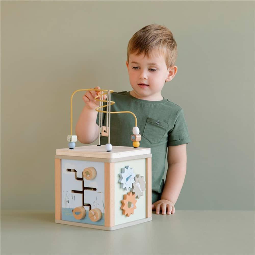 niño de pie con camiseta verde jugando tras un cubo de actividades de madera con diferentes ejercicios para trabajar la motricidad fina, como laberintos, encajares, diagramas en preciosos colores azules, mostaza y verdes