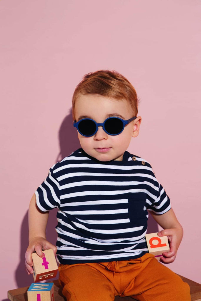foto de lifestyle de niño con camiseta re rayas blancas y azules y Gafas de sol infantiles marca izipizi en talla 3 5 años, montura modelos d , redondeadas en color azul marino